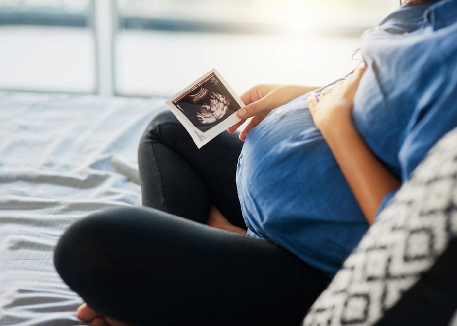 A pregnant person sitting cross-legged holding a photo of her sonogram